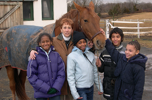 一个大人和三个孩子站在一匹马前面。